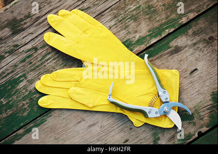 Gelbe Gummihandschuhe und Garten Astschere auf hölzernen Hintergrund. Closeup. Stockfoto