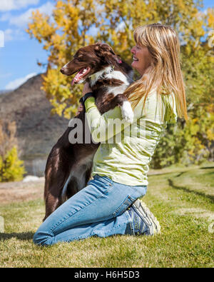 Attraktive Frau spielt mit ihrem Border-Collie Hund auf einer Wiese Stockfoto