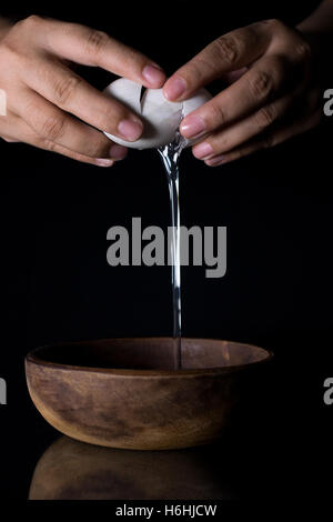 Nahaufnahme der Hände krachend Ei und Holz Schüssel auf schwarz Stockfoto