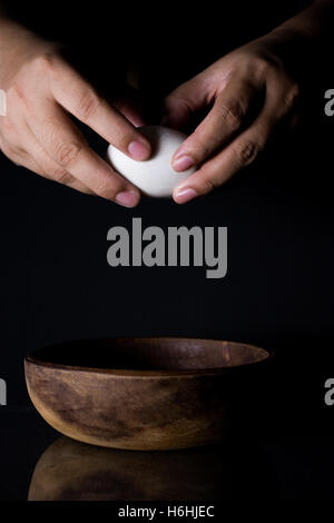 Nahaufnahme der Hände krachend Ei und Holz Schüssel auf schwarz Stockfoto