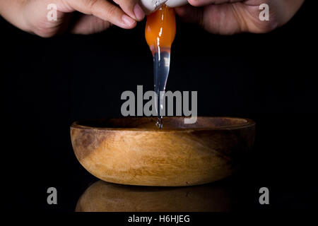 Nahaufnahme der Hände krachend Ei und Holz Schüssel auf schwarz Stockfoto