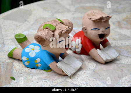 Lehm-Puppen Kinder Jungen und Mädchen Lesebuch am Steintisch im Garten Stockfoto