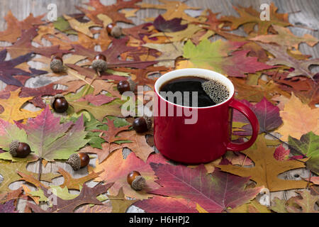 Selektiven Fokus auf eine große rote Tasse heißen dunklen Kaffee mit lebendigen Herbst Blätter auf rustikalen Holz. Stockfoto