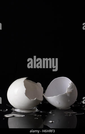 Weisse Eierschalen auf schwarzem Hintergrund mit Wassertropfen und Reflexion isoliert geknackt. Stockfoto