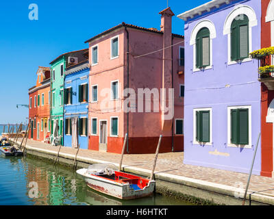 Typische farbige Esterior Fassaden entlang Burano Straßen und Kanälen, mit angedockten Schiffe und Venedig im Hintergrund. Stockfoto