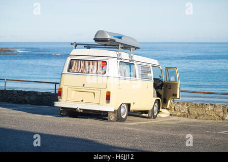 Ein Oldtimer Volkswagen Bulli camping Bus Sennen Cove Beach Car Park mit Blick auf das blaue Meer in der Morgensonne im Sommer, Cornwall, UK Stockfoto