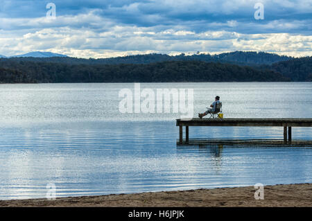 Fischer saß auf dem Steg am Wallaga Lake am Abend, in der Nähe von Bermagui, New-South.Wales, Australien Stockfoto