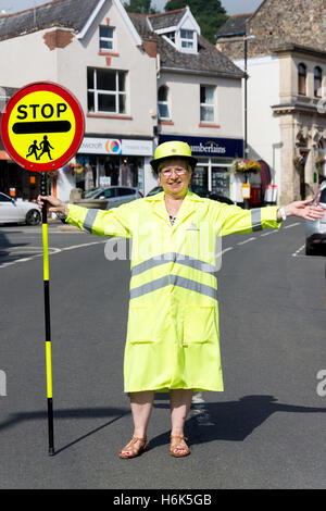 Lollipop-Dame (Schule Kreuzung Patrol Officer) stoppen Verkehr auf Vorderstraße, Bovey Tracey, Devon, England, Vereinigtes Königreich Stockfoto