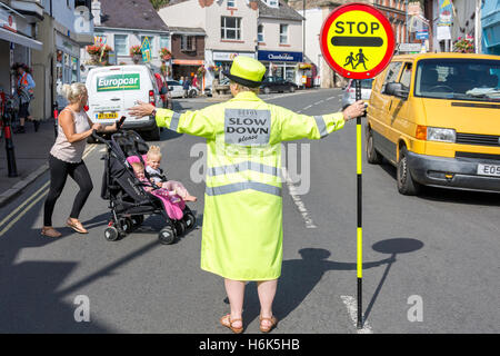 Lollipop-Dame (Schule Kreuzung Patrol Officer) stoppen Verkehr auf Vorderstraße, Bovey Tracey, Devon, England, Vereinigtes Königreich Stockfoto