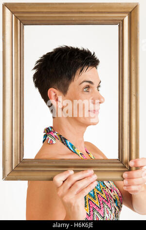 Obere Ansicht eine schwarzhaarige Frau mittleren Alters mit vergoldeten Bilderrahmen vor weißem Hintergrund. Stockfoto