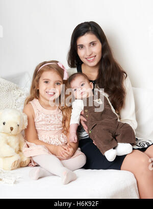 Mutter mit ihren Kindern sitzen im Bett mit Teddybär, glückliche Familienbild Stockfoto