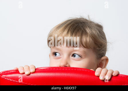 kleines Mädchen schaut verschmitzt hinter dem Stuhl Stockfoto