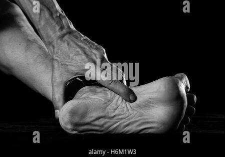 Schmutzige Hand sucht Splitter in schmutzigen Fuß stecken. Stockfoto