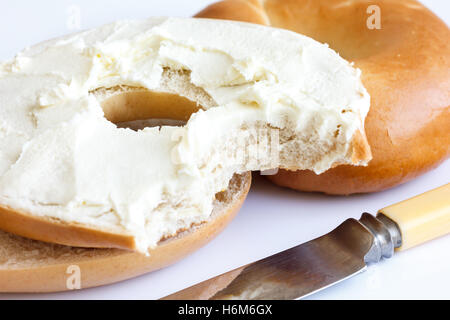 Plain Bagel mit Messer, mit Frischkäse bestreichen und Biss fehlt, Detail. Stockfoto