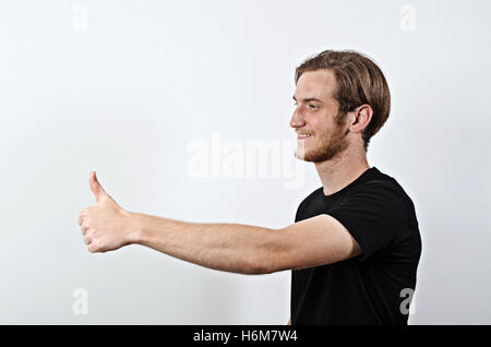 Lächelnde junge Männchen in dunkles T-Shirt zeigt seine Daumen Stockfoto