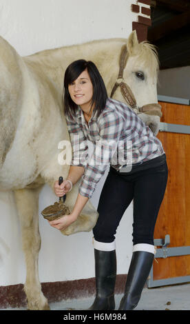 schöne Brünette junge Frau reinigt den Pferdehufen Stockfoto
