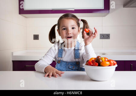 Kleines Mädchen mit Kirsche Birne Tomaten in ihrer Hand. Aufklärung über gesunde Ernährung für Kinder Stockfoto