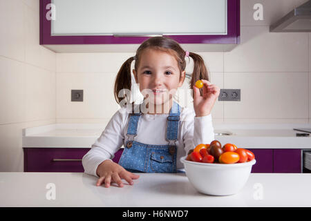 Kleines Mädchen mit gelben runden Cherry-Tomate in der Hand. Aufklärung über gesunde Ernährung für Kinder Stockfoto