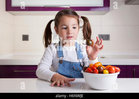 Kleines Mädchen mit Kirsche Kumato Tomaten in ihrer Hand. Aufklärung über gesunde Ernährung für Kinder Stockfoto