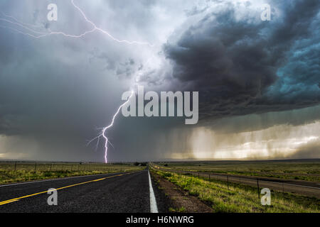 Ein heller Blitz, der während eines Sturms in der Nähe von Springer, New Mexico, über einer langen Straße einstürmt Stockfoto