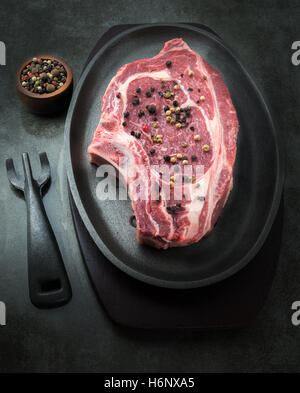 vertikales dunkel und stimmungsvolle Bild eines rohen saftige Steaks mit einem kleinen Topf mit Pfefferkörnern im Hintergrund. Raum für Textfreiraum Stockfoto