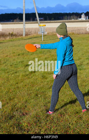 Junge Frau wirft CD zum Ziel auf Disc-Golf-Kurs. Stockfoto