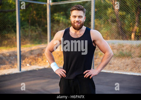 Glücklich Jüngling in Sportbekleidung stehend mit Händen auf Hüften und Blick in die Kamera im freien Stockfoto