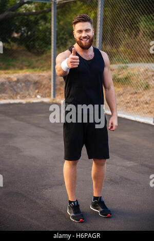 Voller Länge Porträt eines bärtigen happy Fitness zeigt Daumen oben im freien Stockfoto