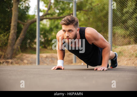 Attraktive bärtiger junger Sportler tun Liegestütze im freien Stockfoto