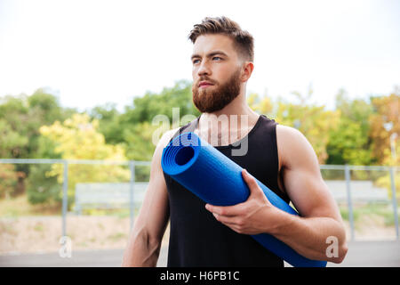 Konzentrierte schwere männliche Yogalehrerin Matte stehen im Freien halten Stockfoto