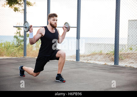 Konzentrierte sich junge bärtige Sportler hockenden Übungen mit Langhantel im freien Stockfoto