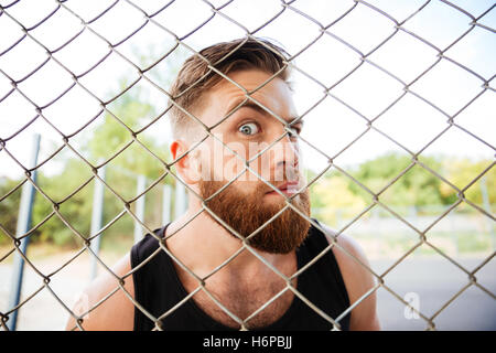 Porträt eines bärtigen lustige Blick durch die Metall-Zaun im freien Stockfoto