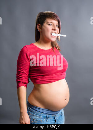 Fröhlich und überrascht Frau mit Schwangerschaftstest im Mund. Stockfoto