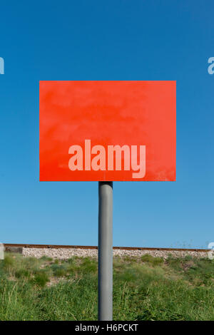 Das zusammengesetzte Bild von leeren roten Schild auf grau Pol mit Bahndamm und Linie im Hintergrund gegen einen klaren blauen Himmel an einem sonnigen Sommer. Stockfoto