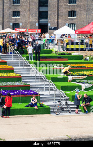 Sonnenanbeter auf die Schritte der Getreidespeicher Square von Regent's Canal in King's Cross, London, UK, geschmückt mit künstlichem Gras und Blumen, 2014 Stockfoto