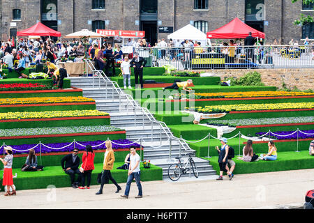 Sonnenanbeter auf die Schritte der Getreidespeicher Square von Regent's Canal in King's Cross, London, UK, geschmückt mit künstlichem Gras und Blumen, 2014 Stockfoto