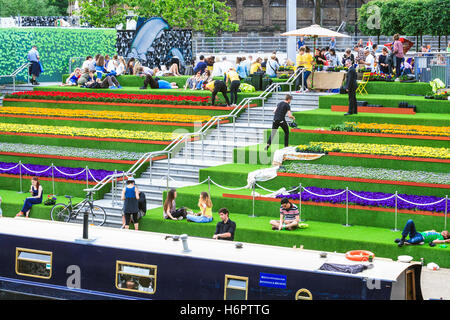 Sonnenanbeter auf die Schritte der Getreidespeicher Square von Regent's Canal in King's Cross, London, UK, geschmückt mit künstlichem Gras und Blumen, 2014 Stockfoto