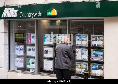 Ein Mann, der an in einem Miller landesweite Immobilienmakler Fenster in Falmouth, Cornwall. Stockfoto