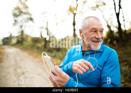 Senior-Läufer in der Natur mit Ihrem Smartphone mit Kopfhörern. Stockfoto
