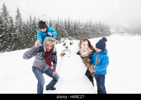 Eltern mit ihren Söhnen, spielen im Schnee, Schneemann bauen. Stockfoto