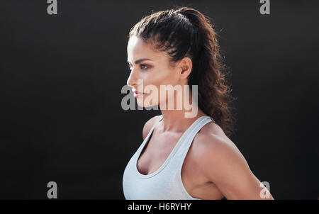 Schuss von attraktive junge Frau in Sportkleidung posiert auf schwarzem Hintergrund hautnah. Gesunde weibliche Modell konzentriert im studio Stockfoto