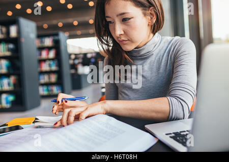 Junge Frau an einem Buch studieren und Abbau Hinweis beim Sitzen am Schreibtisch Bibliothek. Asiatische Studentin Finale vorbereiten Stockfoto