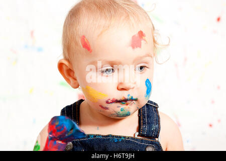 süßes kleines Kind im Overall mit Pinsel und Farben Stockfoto