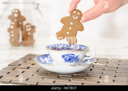 Pfefferkuchen-Mann wird in eine Tasse Tee mit Glas von Cookies im Hintergrund getaucht Stockfoto