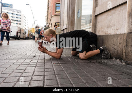 Ein junger männlicher Bettler kniet auf dem Bürgersteig seine Tasse halten, wie er um Geld in Barcelona, Spanien bettelt Stockfoto