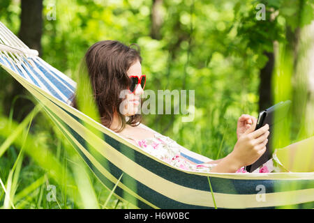junge Frau liegen in der Hängematte im Garten mit e-Book. Stockfoto
