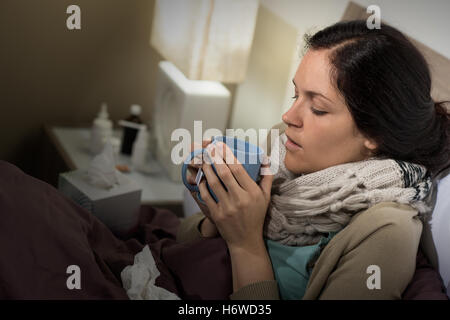 Frau Tasse Tee trinken trinken Lätzchen weibliche Closeup Bett Porträt europäischen kaukasischen Lüge liegenden Lügen Schmerzen Kopfschmerzen Virus Schlafzimmer Stockfoto