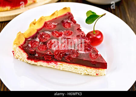 Süße Kuchen mit Kirschen Beeren und Gelee in einem Teller mit einer Gabel auf einem dunklen Holzbrett Stockfoto