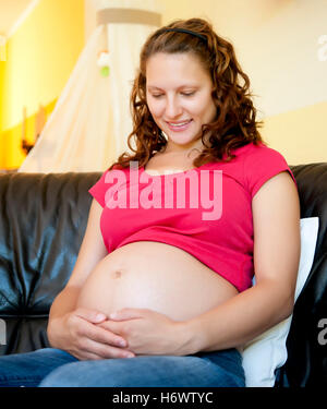 Schwangere junge Frau sitzt auf der couch Stockfoto
