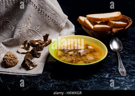 Pilzsuppe in grüne Platte mit Metalllöffel auf einem schwarzen Stein Hintergrund. Einige getrocknete Steinpilze oder weiße Pilze Stockfoto